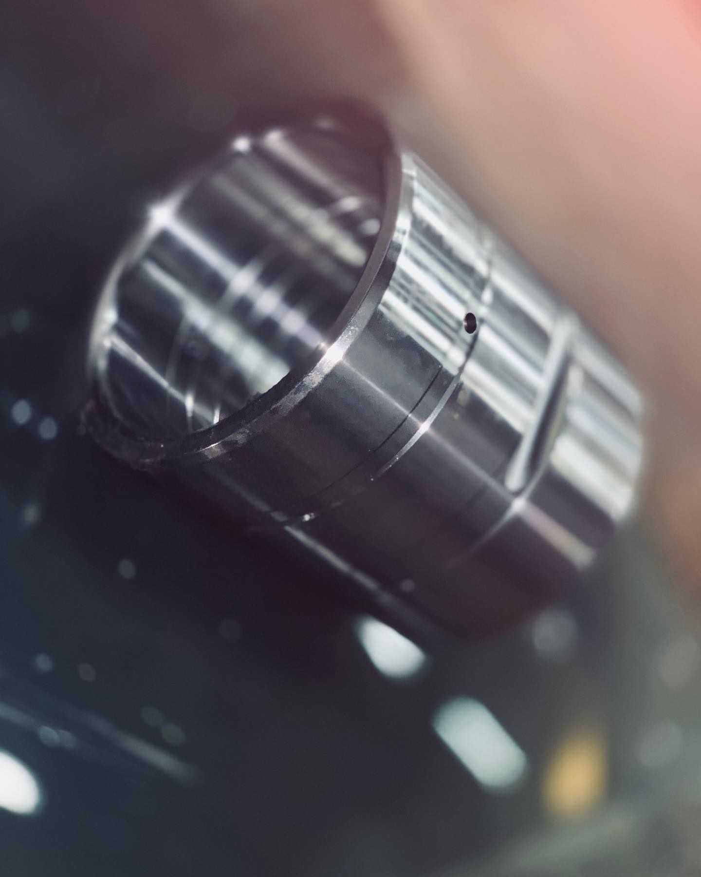 Close-up of a shiny, cylindrical metal object with a blurred background, reflecting surrounding light.